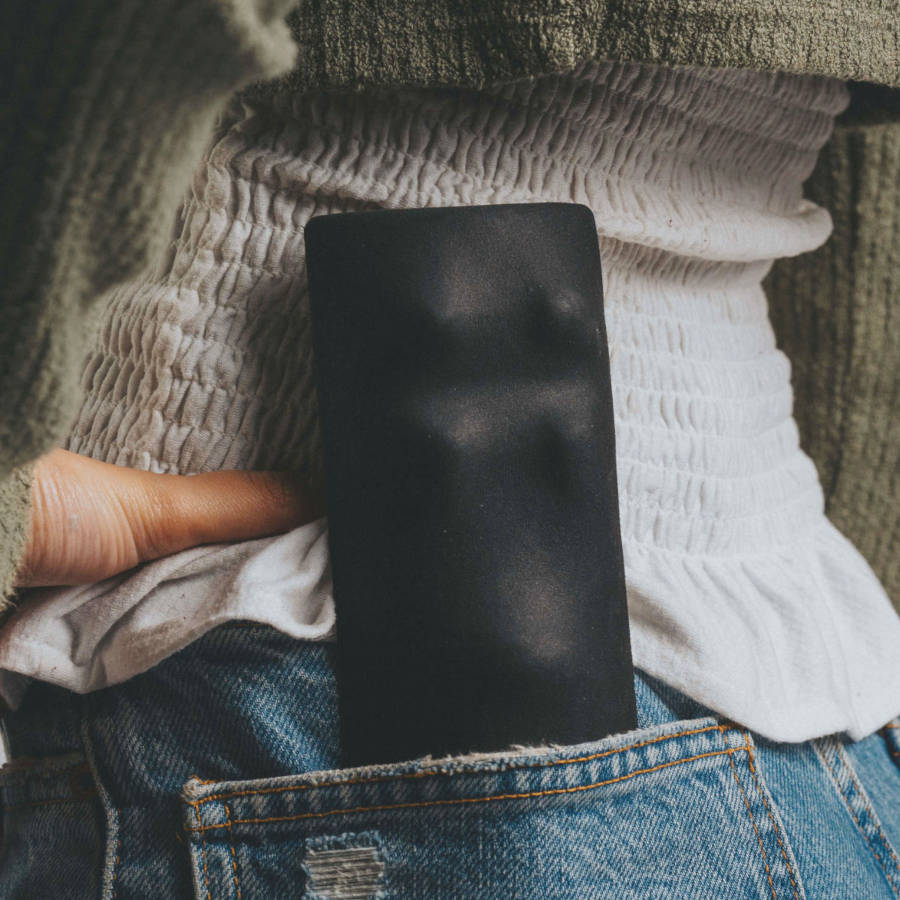 Schwarzes Empelvic-Kissen für das Beckenbodentraining steckt in der Gesäßtasche einer blauen Jeans, Person trägt weiße, strukturierte Bluse und grünen Pullover