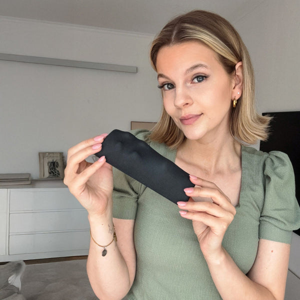 Frau mit kurzen blonden Haaren in grünem Oberteil in einem modernen Wohnzimmer hält den Empelvic Beckenbodentrainer in den Händen 